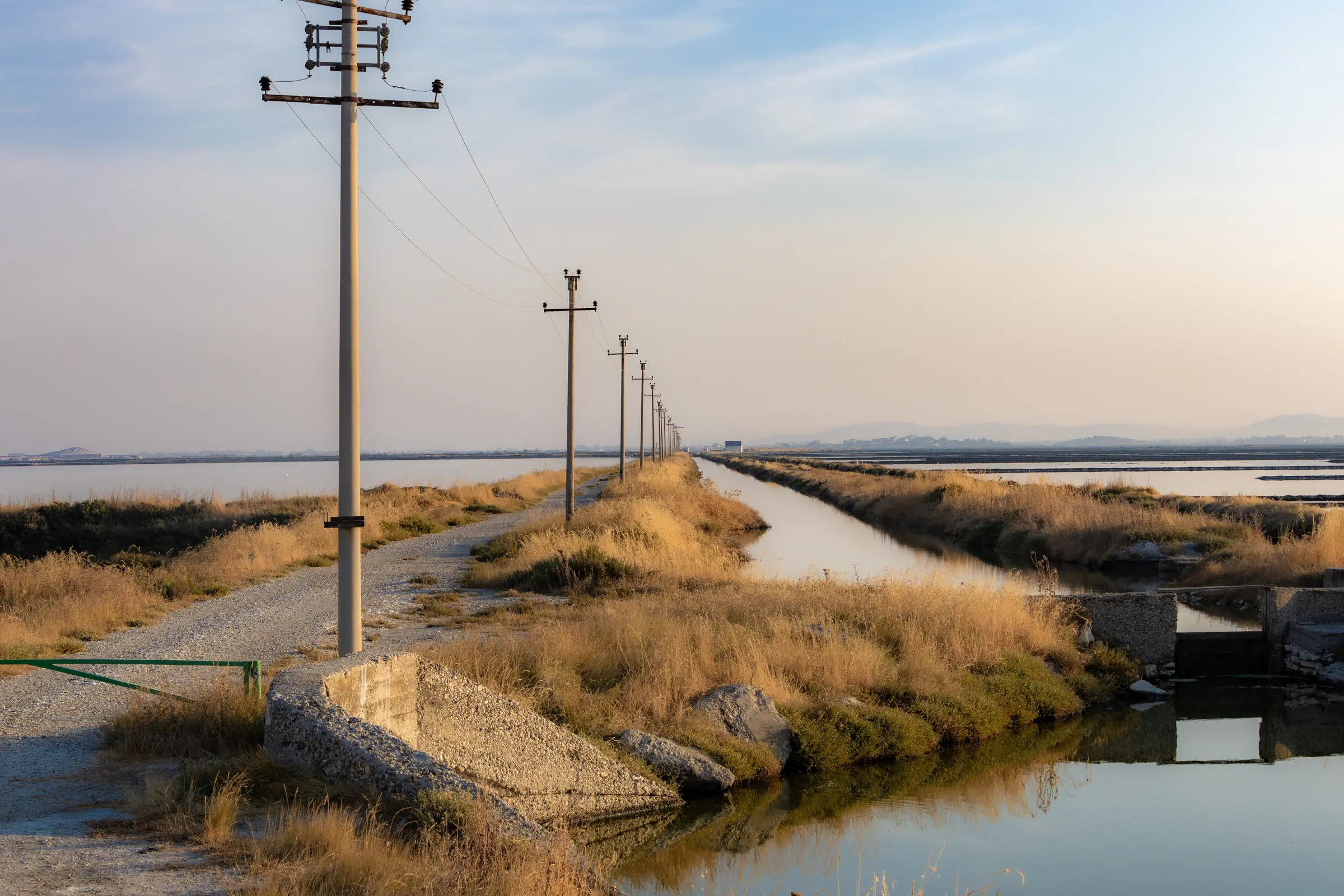 Entwässerungskanal, Betonbauwerk und Strommasten durchziehen die Salinenlandschaft